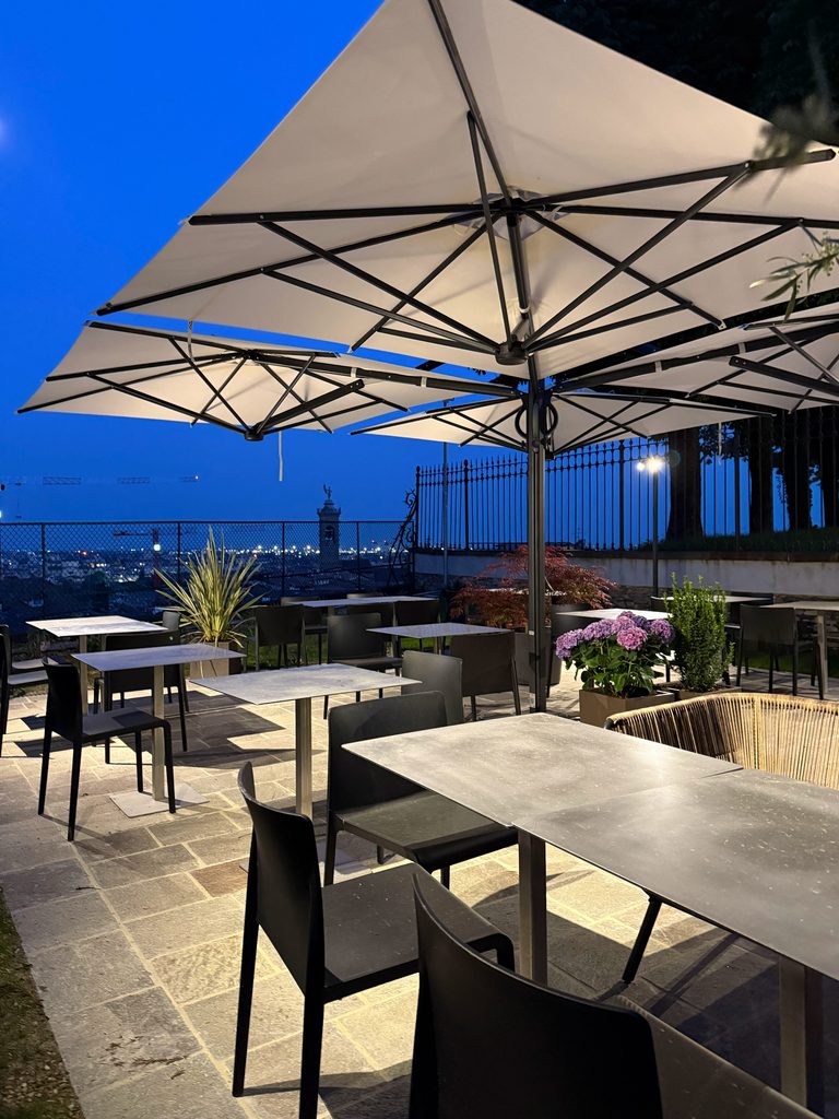 Terrazza serale con ombrelloni illuminati e luci di Bergamo sullo sfondo / Evening terrace with lit umbrellas and Bergamo's lights in the background