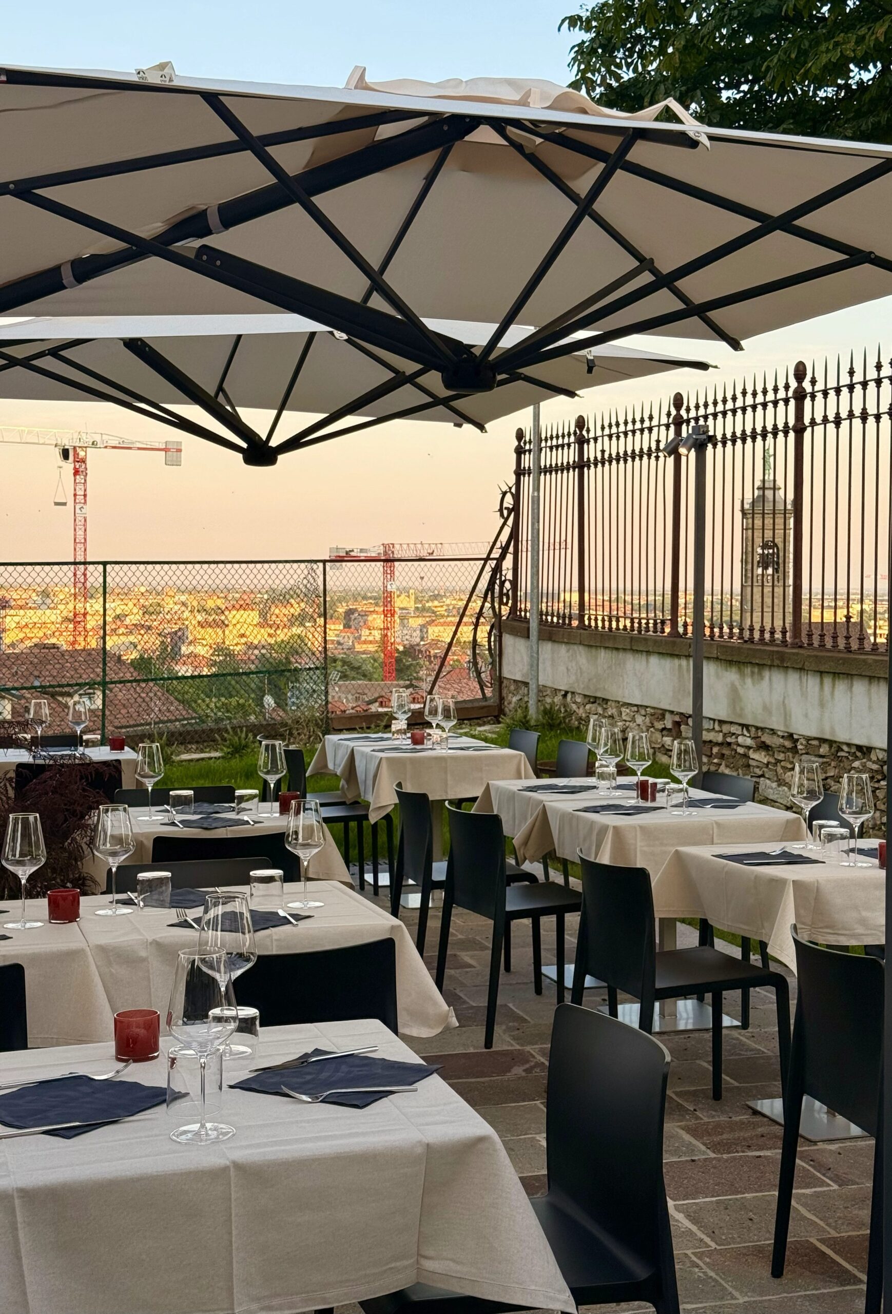 Tavoli apparecchiati al tramonto, tetti di Bergamo bassa sullo sfondo / Tables set at sunset, with Bergamo's rooftops in the background