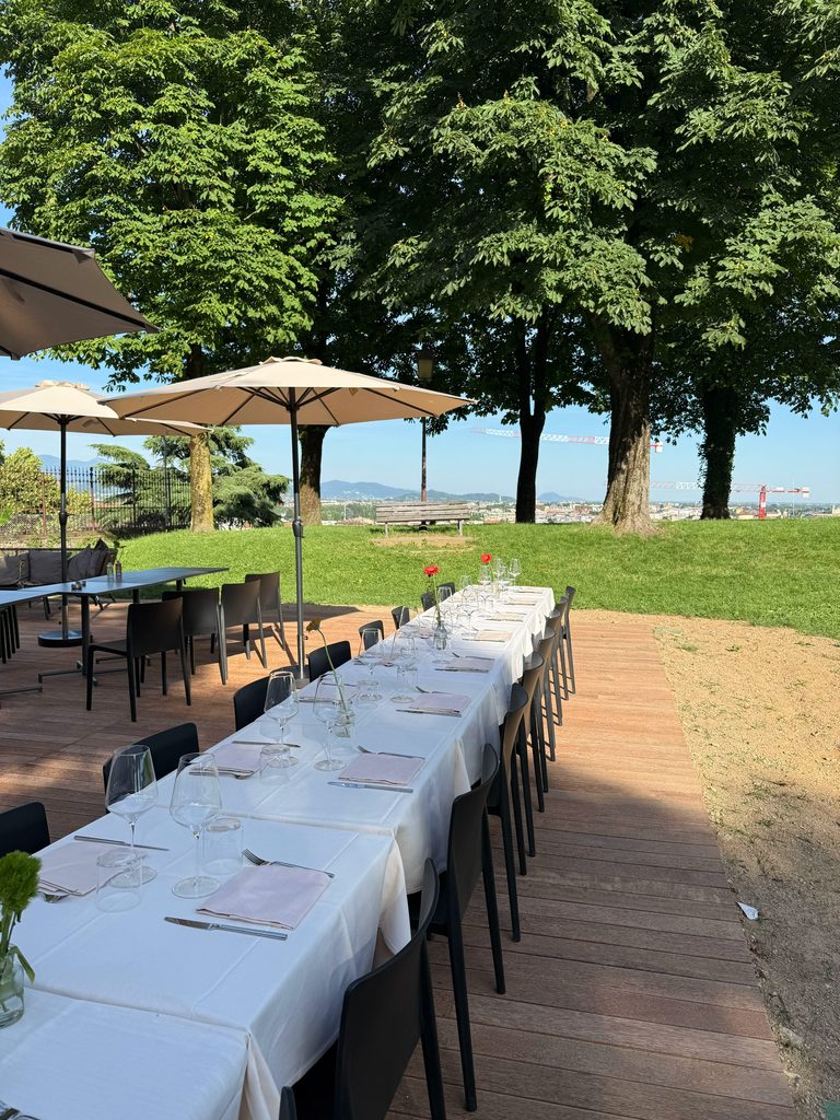 Tavolata lunga apparecchiata sotto gli alberi, vista sulla città / Long table set under the trees, with a view over the city